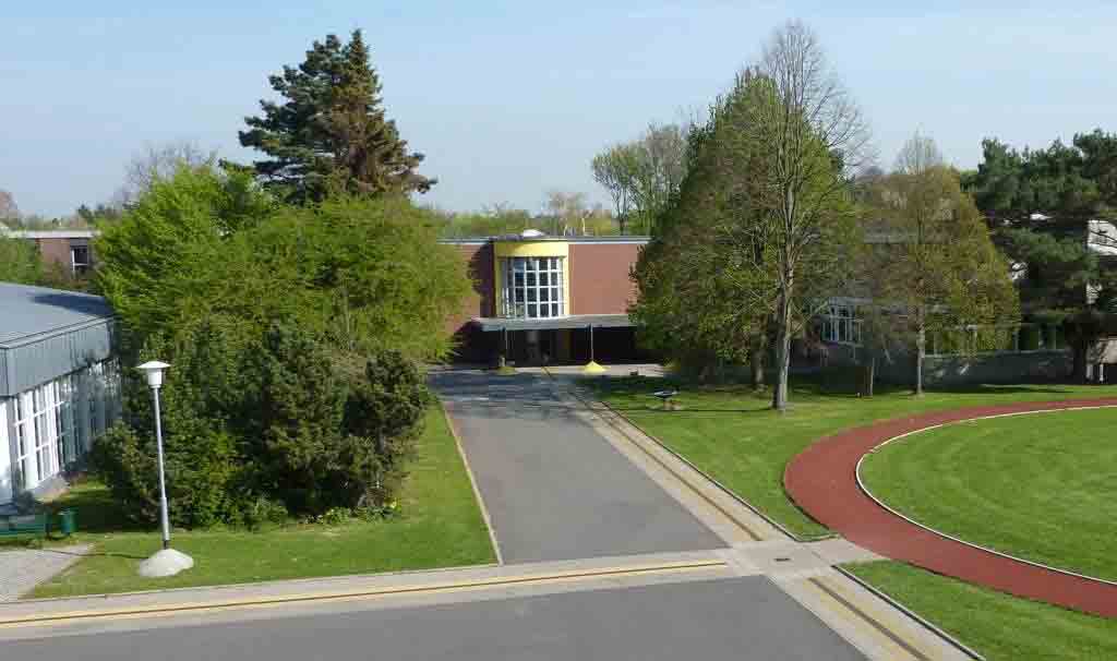 Blick von einem Balkon auf Schwimmbad, Aula und zwei Schulgebäude (von links nach rechts)